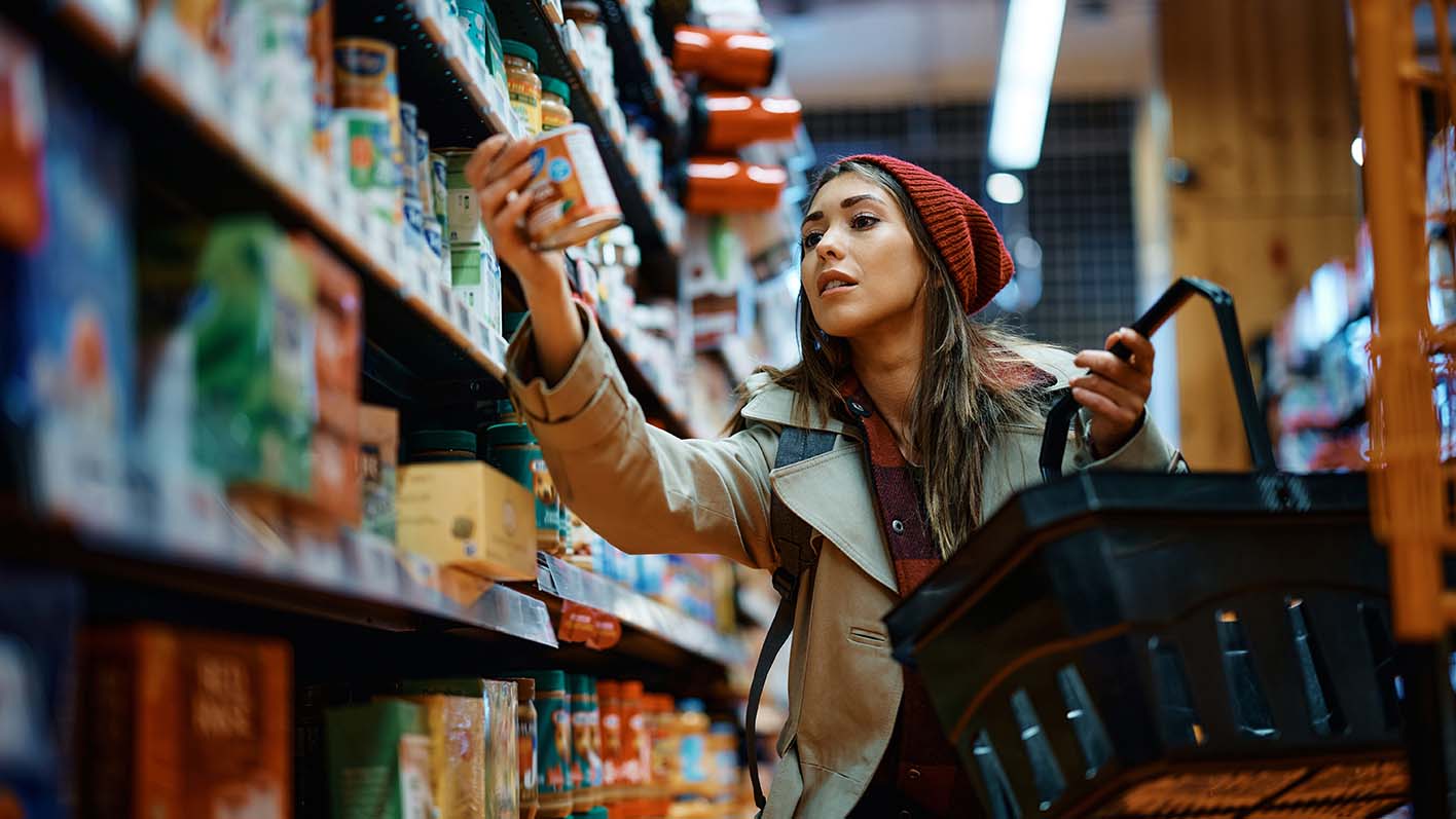 Young woman buying canned food in store.
