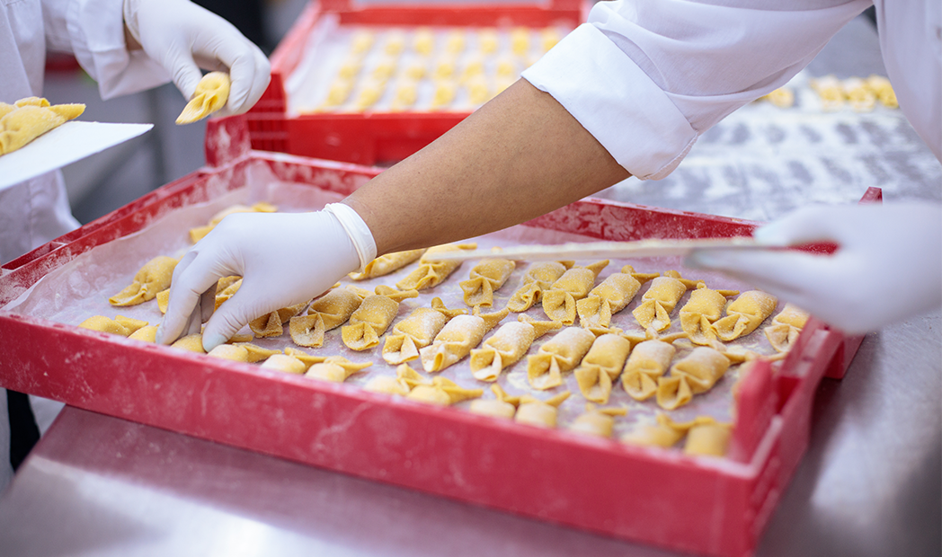 Gloved hands arranging pasta on a tray